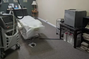 Lotus Laser Aesthetics MedSpa room featuring a treatment bed, laser equipment, and small counter with skincare supplies