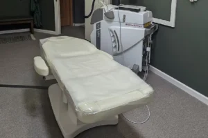 Another Lotus Laser Aesthetics MedSpa room with a padded treatment bed, medical laser device, and a mirror on the wall